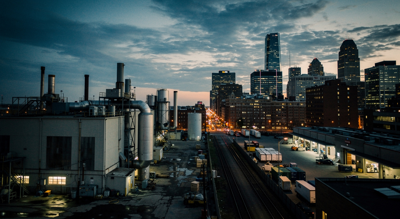 An industrial manufacturing facility and city skyline at dusk, dramatic light